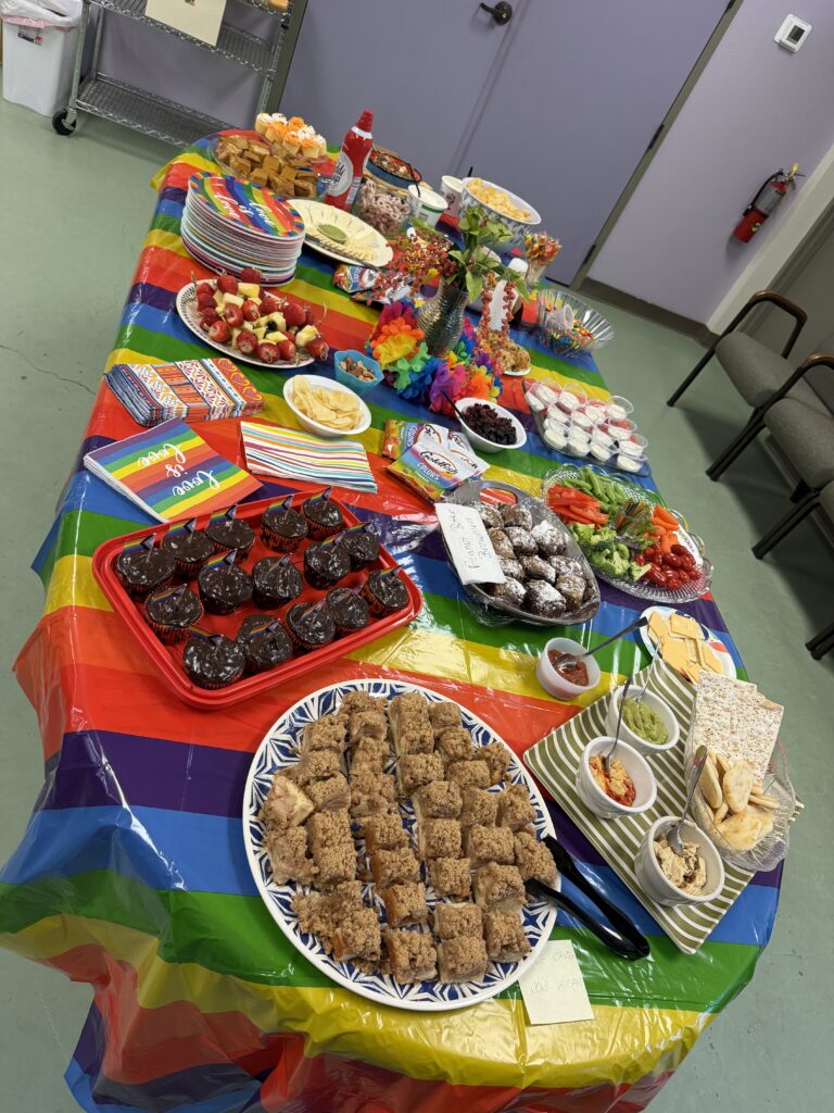 A table covered in a rainbow cloth and filled with snacks and baked treats.