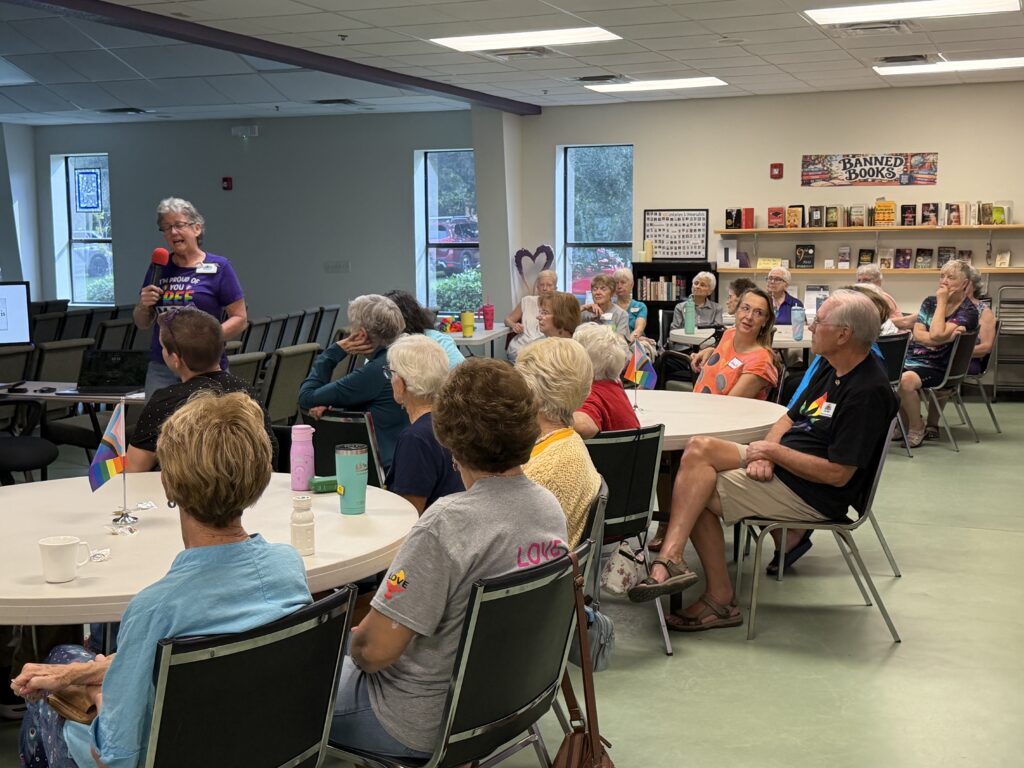 Members at round tables listening to a speaker at the front of the room.