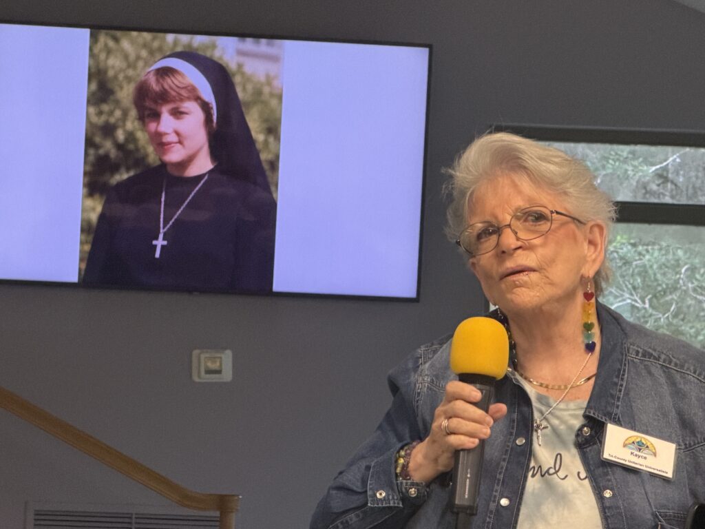A member speaks at the microphone, with an old photograph on the screen behind her.